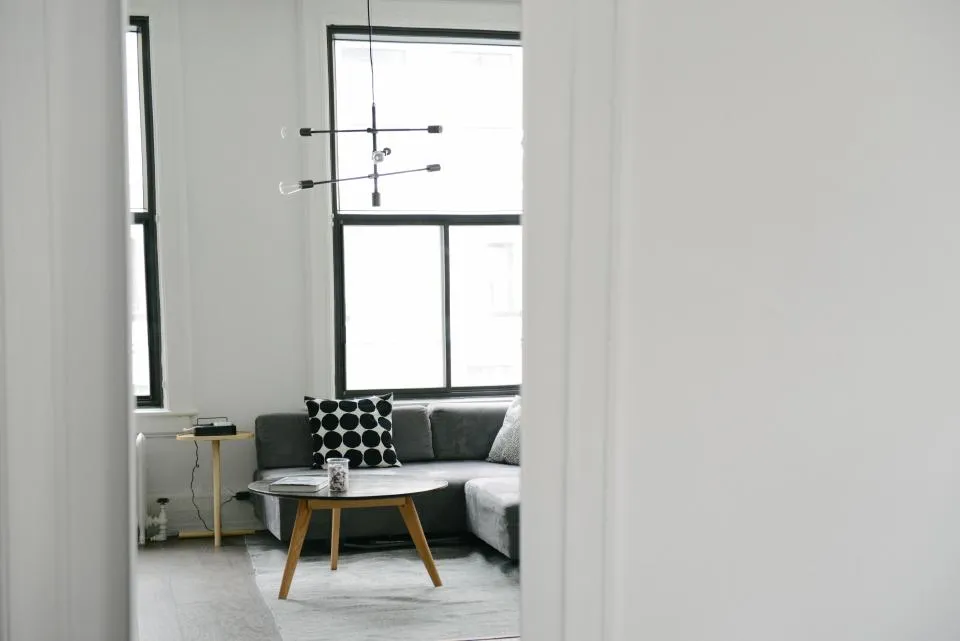 Ein helles, ruhiges Wohnzimmer mit Sofa, rundem Couchtisch und großen Fenstern